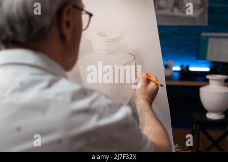 Nahaufnahme von kreativen älteren Mann Hand hält Bleistift Zeichnung Kontur auf Papier Leinwand auf Staffelei im Home Studio. Detail von älteren Künstler freihändig skizzieren Gips Vase Modell in Abendkunst-Workshop. Stockfoto