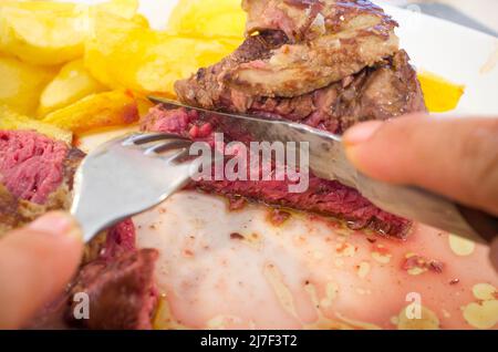 Essen gegrilltes Kalbsfilet mit Gänseleber-Gratin. Hände schneiden Fleisch mit Messer und Gabel Stockfoto