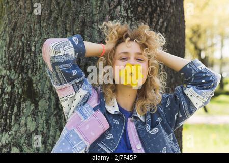 Fröhliches europäisches junges Mädchen mit einer Blume im Mund, die ihr Haar berührt mittlere Nahaufnahme im Freien Wohlbefinden. Hochwertige Fotos Stockfoto