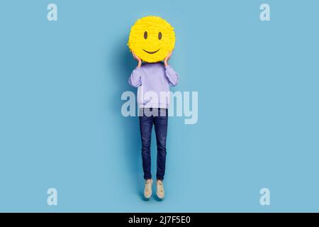 In voller Länge Körpergröße Ansicht der attraktiven fröhlichen Kerl Hippie springen halten Smiley isoliert über hellen blauen Hintergrund Stockfoto