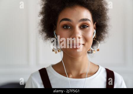 Schwarze junge Frau lächelt, während sie mit Kopfhörern Musik hört Stockfoto