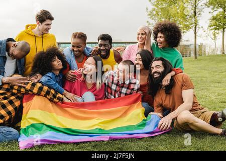 Fröhliche, vielfältige Freunde halten die LGBT-Regenbogenflagge und haben Spaß im Freien - konzentrieren Sie sich auf den richtigen Mann mit Beinprothese Stockfoto