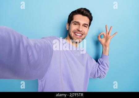 Foto von beeindruckt jungen Brunet Kerl tun Selfie zeigen okey tragen Sweatshirt isoliert auf blauem Hintergrund Stockfoto