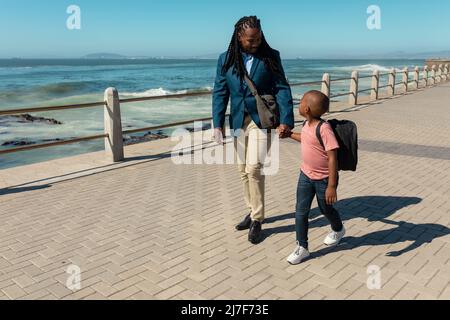 afroamerikanischer Vater und Sohn halten sich die Hände, während sie auf der Promenade spazieren gehen Stockfoto