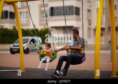 1. Mai 2022, Gaziantep, Türkei: Gaziantep, Türkei. 01 Mai 2022. Der syrische Großvater Kamal Khatib spielt mit seinem Enkelkind auf einem Spielplatz in Gaziantep. Kamal und sein Sohn Bashir wurden getrennt, als Kamal aus dem Krieg floh, um in Jordanien Zuflucht zu suchen. Erst 10 Jahre später, als Kamal in die Türkei reisen konnte, um sich wegen seiner sehr aggressiven Krebsform behandeln zu lassen, kam er mit seinem Sohn wieder zusammen, der jetzt mit seiner Frau und zwei kleinen Kindern in der Türkei lebt. Die Veranstaltung beleuchtet die Tragödie des Krieges in Syrien, bei dem die Syrer in einem nie endenden Konflikt gefangen sind und große Verluste, Vertreibung, und ein verursachen Stockfoto