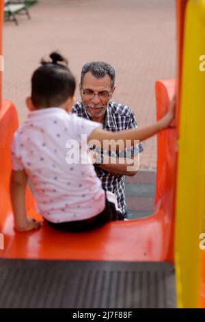 1. Mai 2022, Gaziantep, Türkei: Gaziantep, Türkei. 01 Mai 2022. Der syrische Großvater Kamal Khatib spielt mit seinem Enkelkind auf einem Spielplatz in Gaziantep. Kamal und sein Sohn Bashir wurden getrennt, als Kamal aus dem Krieg floh, um in Jordanien Zuflucht zu suchen. Erst 10 Jahre später, als Kamal in die Türkei reisen konnte, um sich wegen seiner sehr aggressiven Krebsform behandeln zu lassen, kam er mit seinem Sohn wieder zusammen, der jetzt mit seiner Frau und zwei kleinen Kindern in der Türkei lebt. Die Veranstaltung beleuchtet die Tragödie des Krieges in Syrien, bei dem die Syrer in einem nie endenden Konflikt gefangen sind und große Verluste, Vertreibung, und ein verursachen Stockfoto