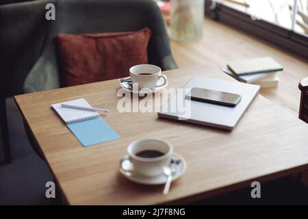 Arbeiten Sie im Café. Tisch mit zwei weißen Kaffeetassen und Business-Sachen. Gemütlicher Ort. Laptop und Smartphone Stockfoto