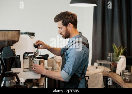 Mann Barista peitschte Milch mit Dampf der Maschine im Krug Stockfoto