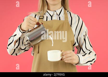 Weibliche Barista gießen Milch auf rosa Hintergrund Stockfoto