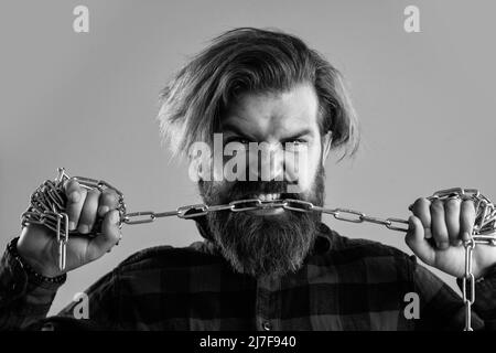 Brutaler bärtiger Mann beißt Stahlkette mit starken Zähnen, Bisskorrektur Stockfoto