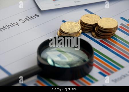 Analyse von Daten, Karten und Grafiken mit Lupe und Goldmünzen Hintergrund. Geschäftsfinanzen und Rechnungslegungskonzept Stockfoto