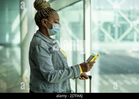 Afrikanische ältere Frau im Flughafenterminal mit Gepäck, das während einer Coronavirus-Pandemie eine Gesichtsmaske trug Stockfoto