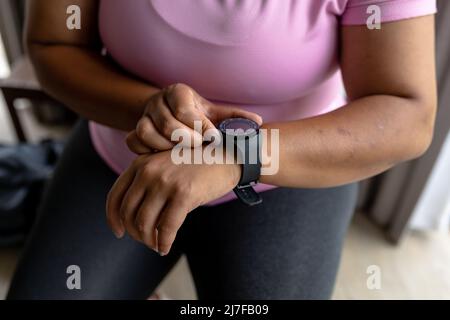 Mittelteil einer afroamerikanischen Frau mit mittlerem Erwachsenen, die die Zeit überprüft, während sie zu Hause sitzt Stockfoto