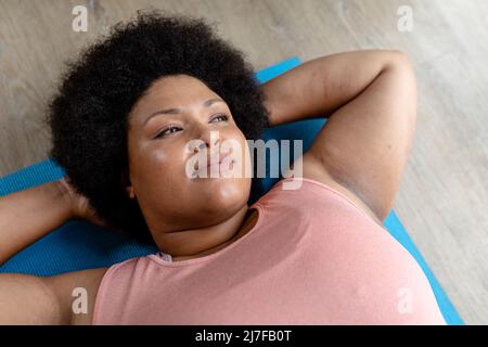 Blick aus der Ferne auf eine afroamerikanische Frau mittlerer Erwachsenen, die auf einer Yogamatte entspannt Stockfoto