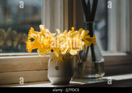 Vase mit gelben Narzissen auf einer alten Fensterbank, Foto in dunklen Farben Stockfoto