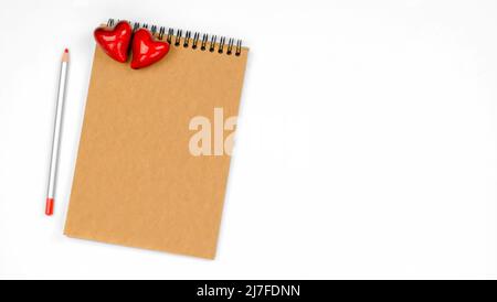 Leerer Notizblock mit Kraftpapier und einem Bleistift auf weißem Hintergrund mit Herzen. Das Konzept des Valentinstag, Muttertag. Nachahmung zur Gratulation Stockfoto