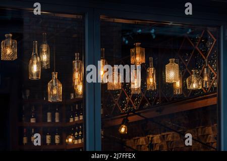 Laternen aus Glasflaschen und Edison-Glühlampen. DIY-Lampen aus recycelten alten Flaschen, die im Café-Fenster hängen Stockfoto