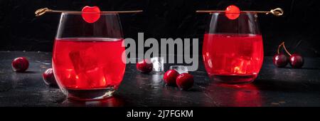 Cocktail garniert mit Kirschpanorama, frischem Preiselbeersaft mit Eis auf dunklem Grund, zwei Gläsern, einem Panorama-Banner Stockfoto