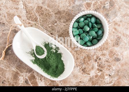 Pulver- und Spirulina-Tabletten in Schalen auf einem Marmortisch. Draufsicht. Superfood, Nahrungsergänzungsmittel. Quelle von Vitamin-Protein und Beta-Carotin Stockfoto