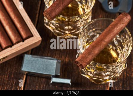 Ansicht einer Holzkiste mit kubanischen Zigarren, einem Feuerzeug und einem Cutter. Stillleben mit zwei Gläsern Whisky auf dem Tisch. Stockfoto