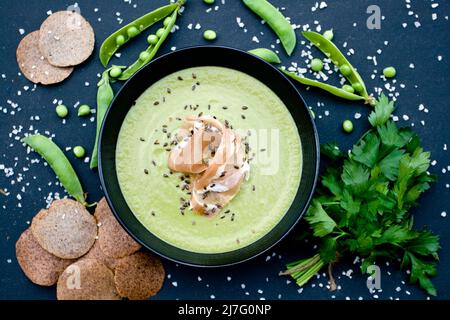 Gesunde grüne Suppe mit Schinken und Erbsen auf schwarzem Hintergrund Stockfoto