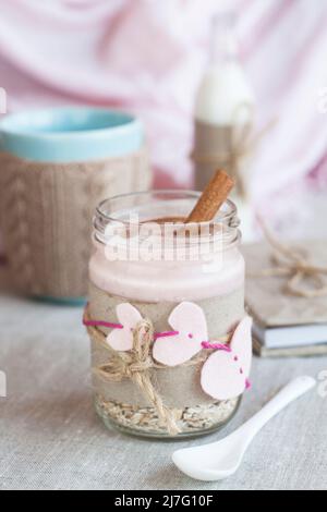 Haferflocken, gewürzt mit Joghurt, bestreut mit Zimt in einem Glas. Als nächstes gibt es eine Tasse Kaffee und eine Flasche Milch. Als nächstes kommt ein Bastelbuch und ein pi Stockfoto