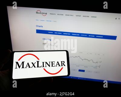 Person, die Mobiltelefon mit dem Logo des amerikanischen Hardwareunternehmens MaxLinear Inc. Auf dem Bildschirm vor der Business-Webseite hält. Konzentrieren Sie sich auf die Telefonanzeige. Stockfoto