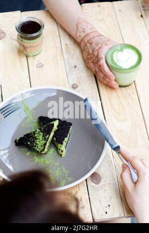 Tasse Matcha Grüner Tee in Frauenhand und Kuchen und Eis mit grünem Matcha Stockfoto