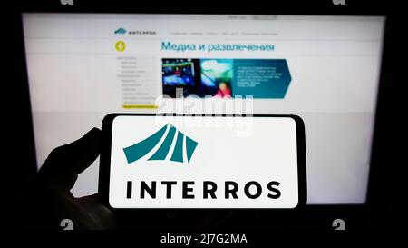 Person, die Mobiltelefon mit dem Logo des russischen Konglomerats Interros auf dem Bildschirm vor der Business-Webseite hält. Konzentrieren Sie sich auf die Telefonanzeige. Stockfoto