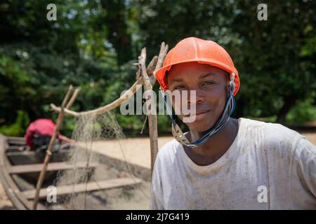 Porträt eines afrikanischen Fischers, der Schutzhelm trägt und mit einem Fischernetz auf seinem Boot sitzt, einer arbeitenden Person am Arbeitsplatz Stockfoto