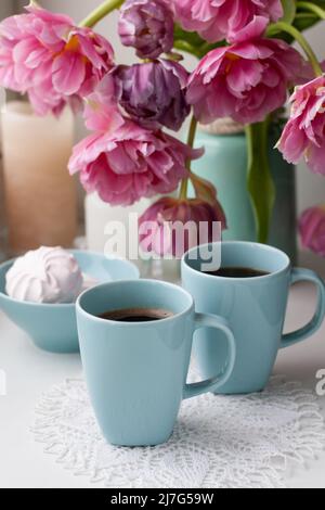 Zwei Tassen schwarzen Kaffee und ein zartes Marschlauch zum Frühstück stehen neben einem schönen Bouquet aus rosa Tulpen in einer blauen Vase. Stockfoto