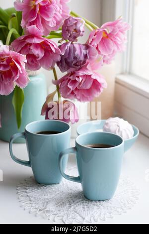 Zwei Tassen schwarzen Kaffee und ein zartes Marschlauch zum Frühstück stehen neben einem schönen Bouquet aus rosa Tulpen in einer blauen Vase. Stockfoto