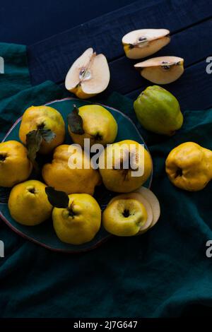 Gelbe herbe Quitte liegt auf einem dunklen Teller auf einem natürlichen Tuch auf einem schwarzen Holzhintergrund. Eine Frucht wird geschnitten. Stockfoto