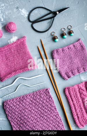 Draufsicht: strickzubehör und Muster von Strickwaren liegen auf grauem Betongrund. Platz für die Beschriftung. Stockfoto