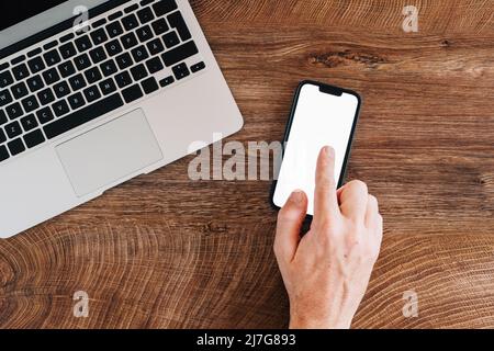 Tippen Sie mit der Hand auf den Smartphone-Mockup-Bildschirm, und betrachten Sie den flachen Arbeitsplatz im Home Office von oben Stockfoto