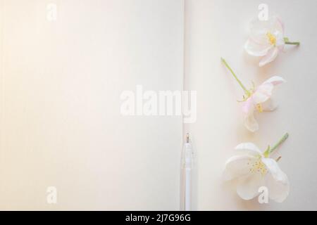 Offenes Buch mit leeren Blättern, Feder- und Apfelbaumblumen, Flatlay, Kopierraum. Stockfoto