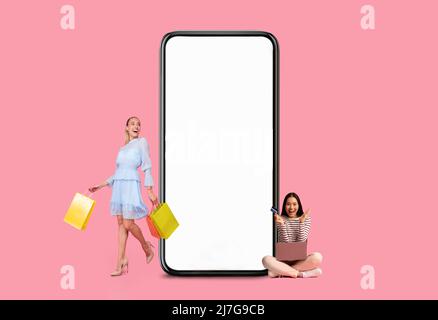 Frauen posieren mit weißem leerem Smartphone-Bildschirm und Einkaufstaschen Stockfoto