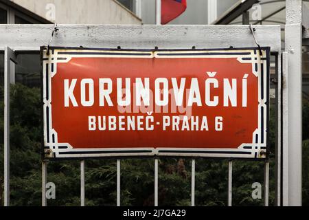 Straße Korunovační. Traditionelles rotes Straßenschild auf dem Gebäude der konsularischen Abteilung der russischen Botschaft im Stadtteil Bubeneč in Prag, Tschechische Republik. Im April 2022 wurde der Teil der Korunovační Straße, auf dem sich die Gebäude der russischen Botschaft befinden, in Ukrainische Heldenstraße (Ukrajinských hrdinů) umbenannt, um gegen die russische Invasion in der Ukraine im Jahr 2022 zu protestieren. Stockfoto