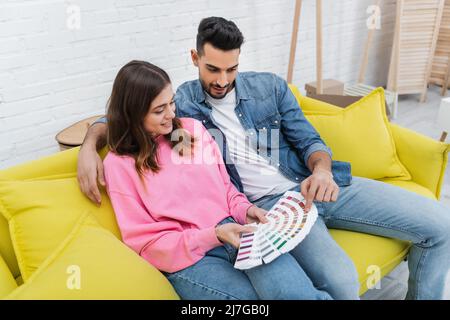 Arabischer Mann zeigt auf Farbpalette in der Nähe der Freundin auf der Couch zu Hause Stockfoto