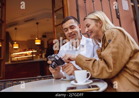 Lächelnder Mann und Frau, die Kaffee genießen und Fotos auf der Retro-Kamera anschauen Stockfoto