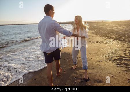 Das ganze Paar hat Spaß, während man barfuß am Sandstrand entlang läuft Stockfoto
