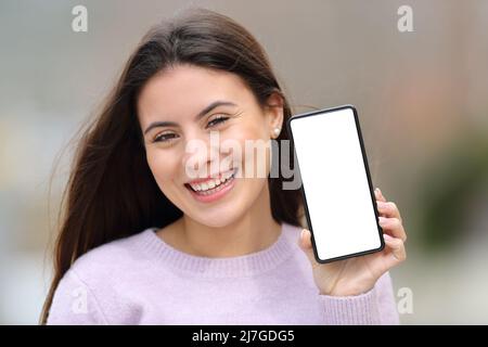 Vorderansicht Porträt eines glücklichen Teenagers, der im Freien auf der Straße einen leeren Telefonbildschirm zeigt Stockfoto