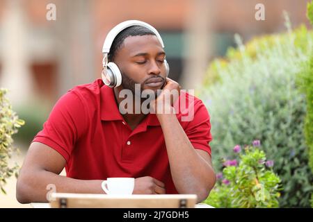 Mann mit schwarzer Haut, entspannende Clossein-Augen, die Musik von Kopfhörern in einer Bar hören Stockfoto