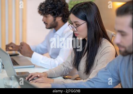 Fokussierte Unternehmensmitarbeiterin und ihre Kollegen, die an ihren Laptops arbeiten Stockfoto
