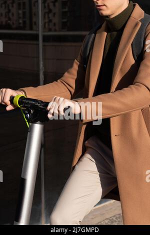 Nahaufnahme der vertikalen Ansicht eines nicht erkennbaren jungen eleganten Mannes, der mit einem Elektroroller durch die Stadt fährt, während er zur Arbeit fährt Stockfoto
