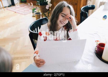 Glückliches Mädchen mit Papier sitzt am Esstisch Stockfoto