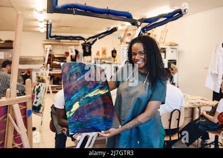 Porträt einer glücklichen Frau mit lockigem Haar, das Malerei in der Kunstklasse zeigt Stockfoto