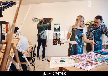 Männliche und weibliche Künstler diskutieren über Gemälde, während der Maler Leinwand an die Wand klebte Stockfoto