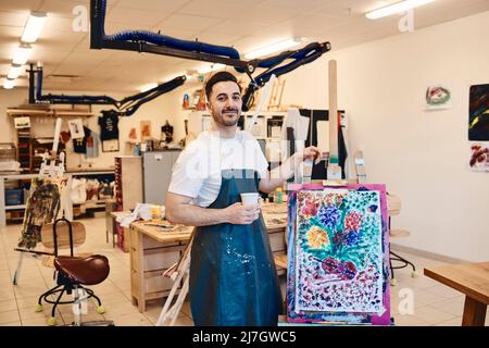 Porträt eines selbstbewussten männlichen Künstlers, der an einer Staffelei mit Malerei in der Kunstklasse steht Stockfoto