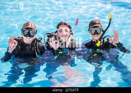 Eine Gruppe glücklicher Taucher lächelt der Kamera mit ihren Tauchmasken und ihrer Ausrüstung in einem Pool zu, der das OK-Schild zeigt Stockfoto